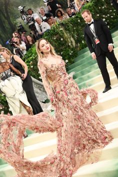 a woman in a floral dress is walking down the stairs at an event with cameras around her