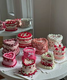 a table topped with lots of cakes covered in pink and red frosting on top of white plates