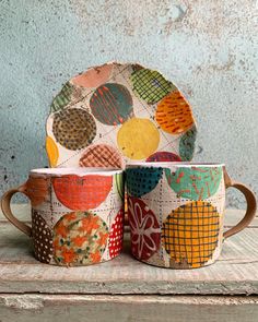 two coffee cups sitting next to each other on top of a wooden table covered in fabric