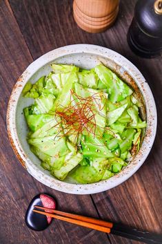 a white bowl filled with lettuce next to chopsticks on top of a wooden table