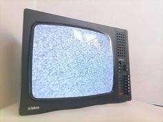 an old television sitting on top of a white table next to a black cordless phone