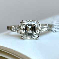 an engagement ring with three baguets on top and a book in the background