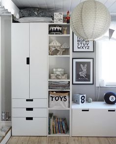 a white bookcase filled with lots of books next to a window and lamp hanging from the ceiling