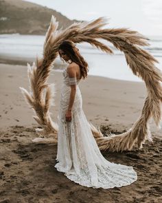 a woman standing on top of a sandy beach next to a large dried grass wreath