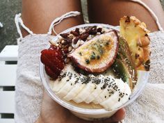 a person holding a bowl of food with bananas, strawberries and other toppings