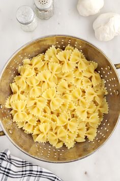 pasta in a colander with garlic and parmesan cheese next to it on a marble countertop