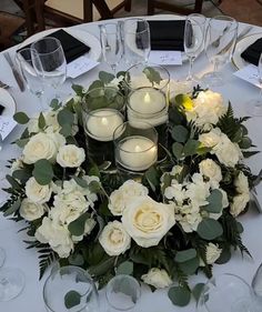 white flowers and candles are arranged on a round table with place settings for guests to sit at