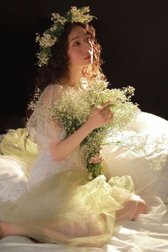 a woman in a white dress sitting on a bed with flowers around her neck and head