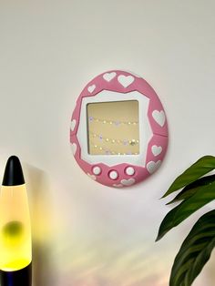 a pink and white wall mounted mirror next to a plant