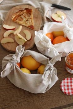 apples, oranges and other fruit on a table with a cloth bag next to them