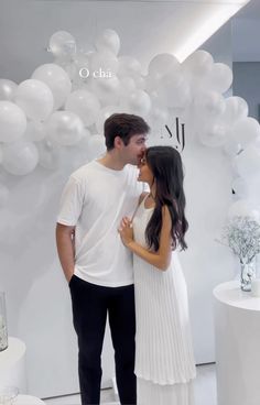 a man and woman standing next to each other in front of white balloons on the wall