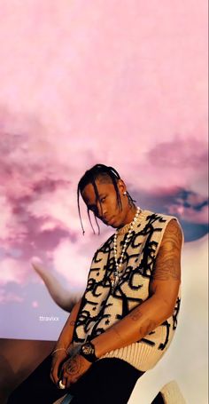 a man with dreadlocks sitting in front of a pink and white sky background