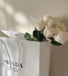 a bouquet of white roses sitting on top of a shopping bag with the word prada written on it