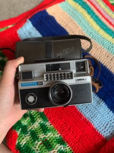 an old camera being held by someone on a colorful blanket in the background is a multicolored rug