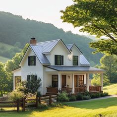 a white house with black shutters on the front and side windows, surrounded by lush green trees