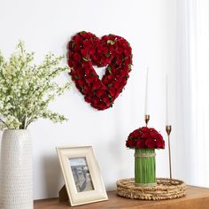 a heart shaped wreath on the wall next to a vase with flowers and a candle