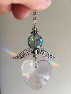 a person holding a heart shaped charm with wings on it's end and a diamond in the middle