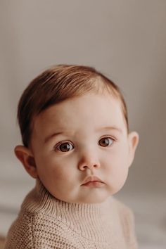 a baby with brown hair wearing a sweater