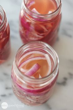 three jars filled with liquid sitting on top of a marble counter topped with red onions