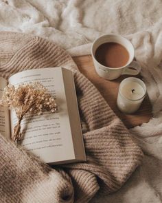 an open book on a bed next to a cup of coffee