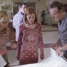 three people looking at a paper model in a room with other people standing around it