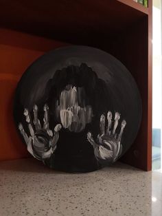 a black and white painting of two hands on a round object in front of a bookshelf