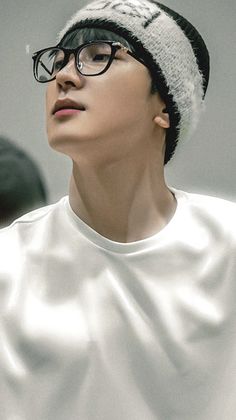 a young man wearing glasses and a white t - shirt looks up at the sky