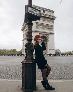 a woman leaning on a lamp post in front of the arc de trioe