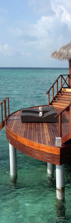 a wooden dock in the middle of clear blue water with a thatched umbrella over it