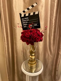 a gold vase with red roses and a movie clapper on it sitting on a table