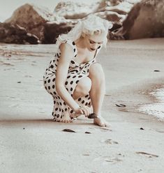 a woman kneeling down on top of a sandy beach