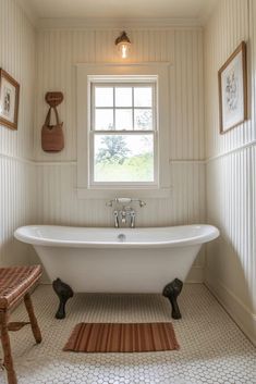 a white bath tub sitting under a window next to a wooden stool in a bathroom