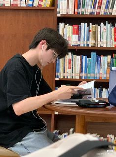 a young man sitting at a table in front of a book shelf while listening to headphones