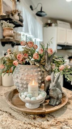 a candle and some flowers in a vase on a tray with rocks, eggs and candlesticks