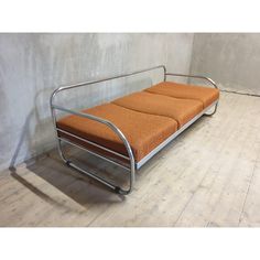 a metal frame futon with an orange cushion on the top and bottom, against a white wall