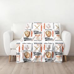 a couch covered in a blanket with baseballs and bats on it, sitting next to a white chair