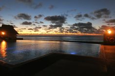 an outdoor swimming pool at night with the sun setting over the water and clouds in the sky