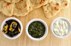 three small white bowls filled with food next to tortillas and sauces on a wooden surface