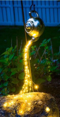 a light up teapot on top of a rock in the garden with lights around it