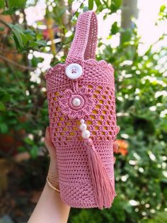 a hand holding a pink crocheted purse with buttons and tassels on it