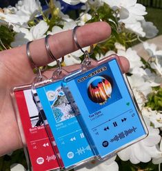 a hand holding two mp3 player keychains in front of flowers