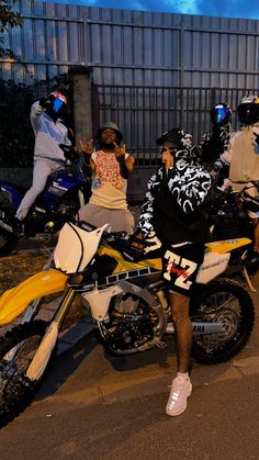 a man standing next to a yellow dirt bike on the side of a road with other people behind him