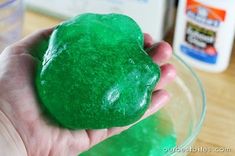 a hand holding a green colored doughnut in a bowl with other ingredients around it