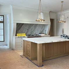 a large kitchen with marble counter tops and gold pendant lights hanging from the ceiling over the island