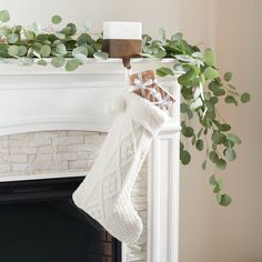 a christmas stocking hanging from a mantel with greenery and candles on it