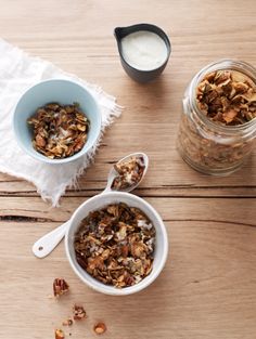 two bowls filled with granola sitting on top of a wooden table next to a glass jar