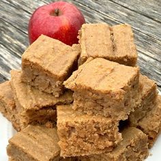 a white plate topped with brownies next to an apple on top of a wooden table