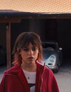 a woman in a red jacket standing next to a car