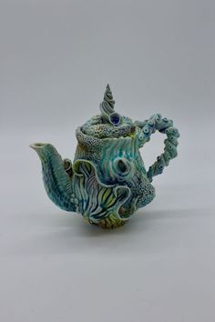 a ceramic teapot with blue and green designs on the outside, sitting on a white surface