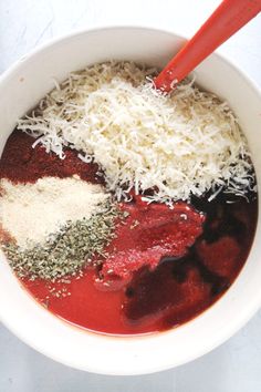 a white bowl filled with different types of spices and seasoning next to a red spoon